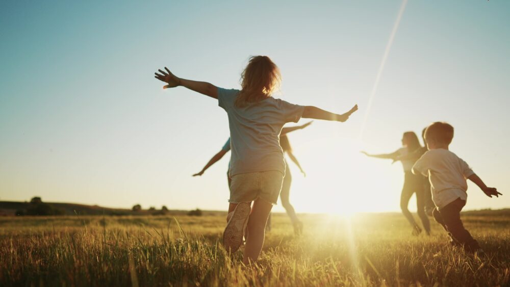 Gesundheit & Nachhaltigkeit / Health & Sustainability: Kinder laufen über eine Wiese im Sonnenuntergang, dies soll an Reflexion, Fokus auf das Wesentliche sowie einen achtsamen Umgang mit sich selbst und der Umwelt erinnern.