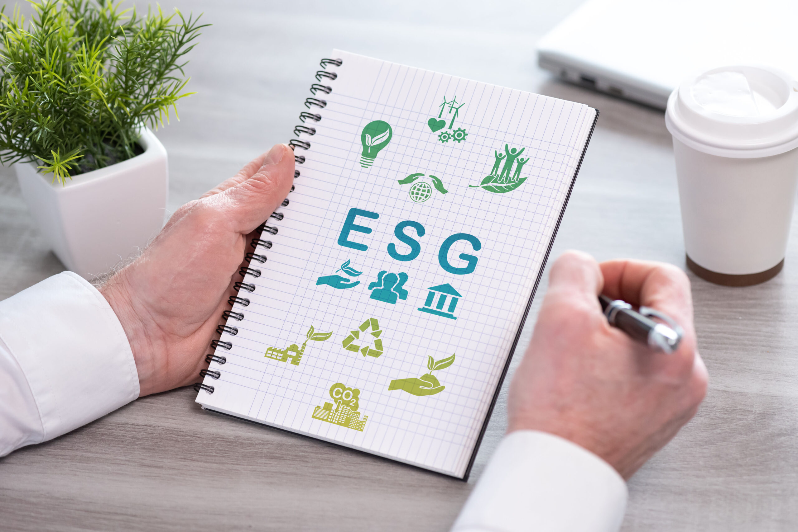 ESG auf Notizblock mit Symbolen, eine Hand hält einen Stift für Notizen; ESG on notepad with symbols, one hand holding a pen for notes